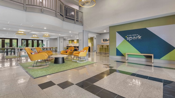 A spacious lobby with a checkered floor, yellow chairs, a green carpet, and a wall with the text "It only takes a spark".