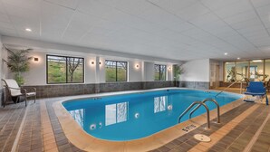 An indoor swimming pool with clear glass walls, a tiled floor, and a few lounge chairs.
