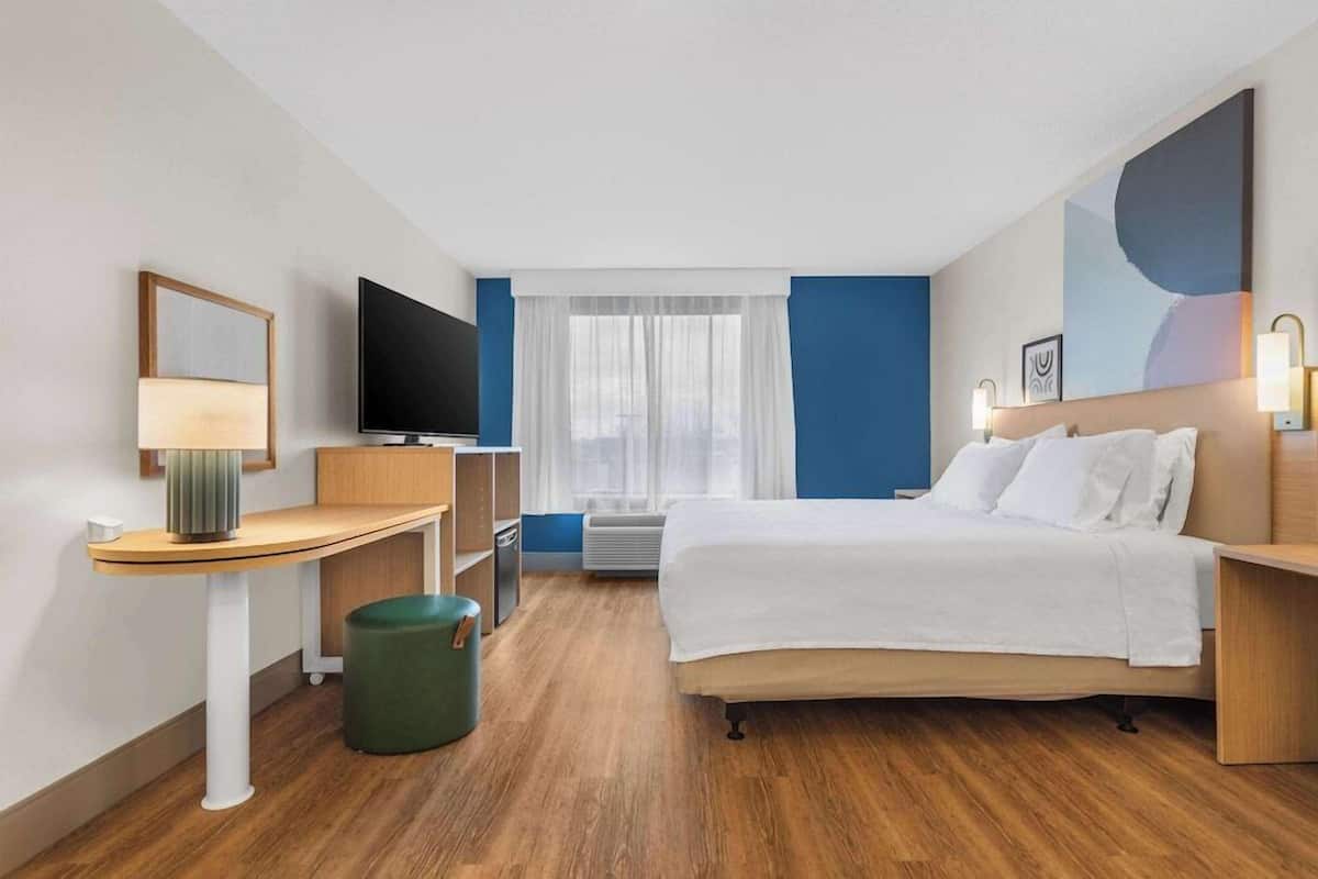 A hotel room with a bed, desk, TV, and a window with curtains.