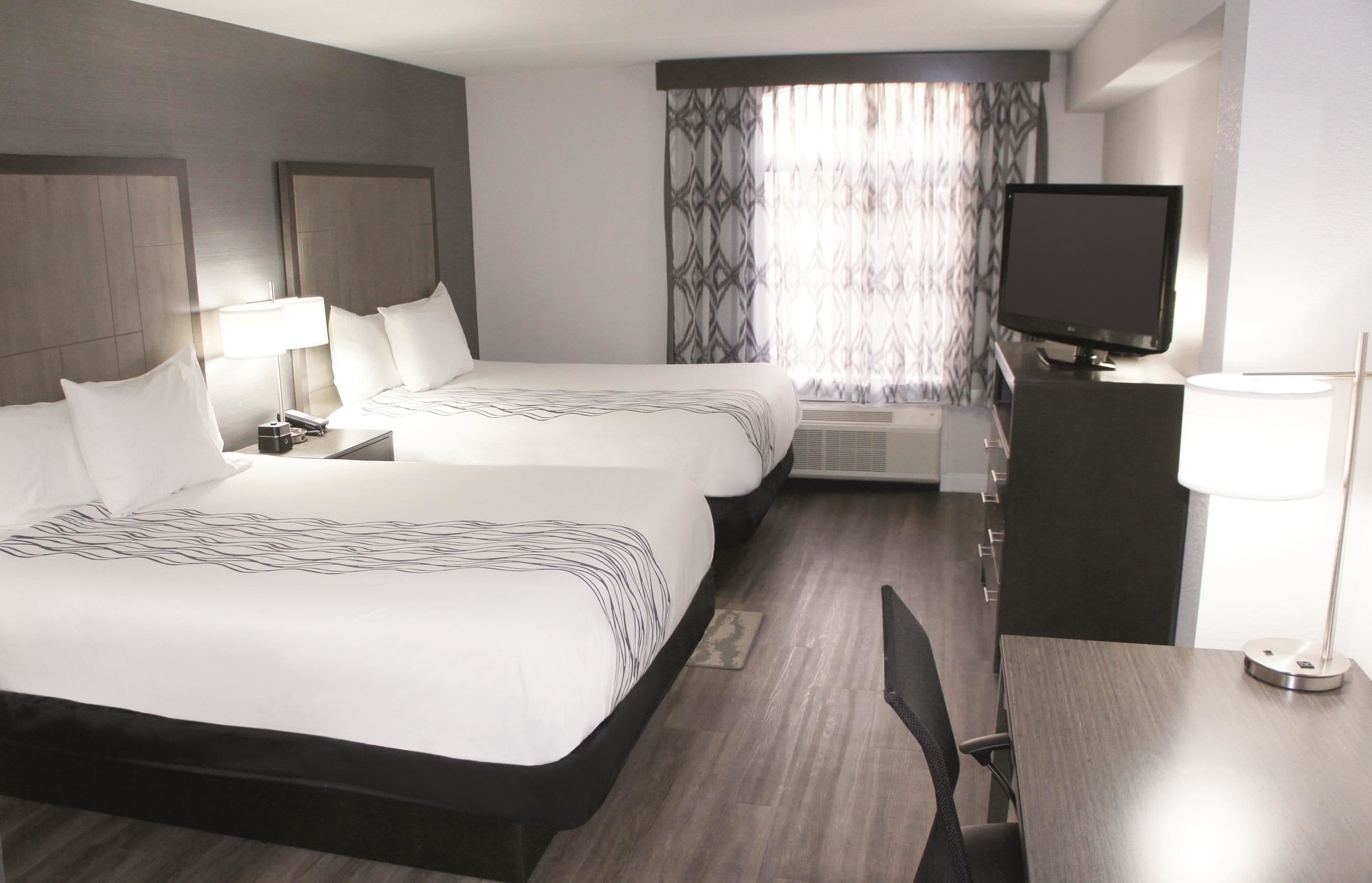 Une chambre d’hôtel avec deux lits, un bureau, une télévision et une fenêtre avec des rideaux à motifs.