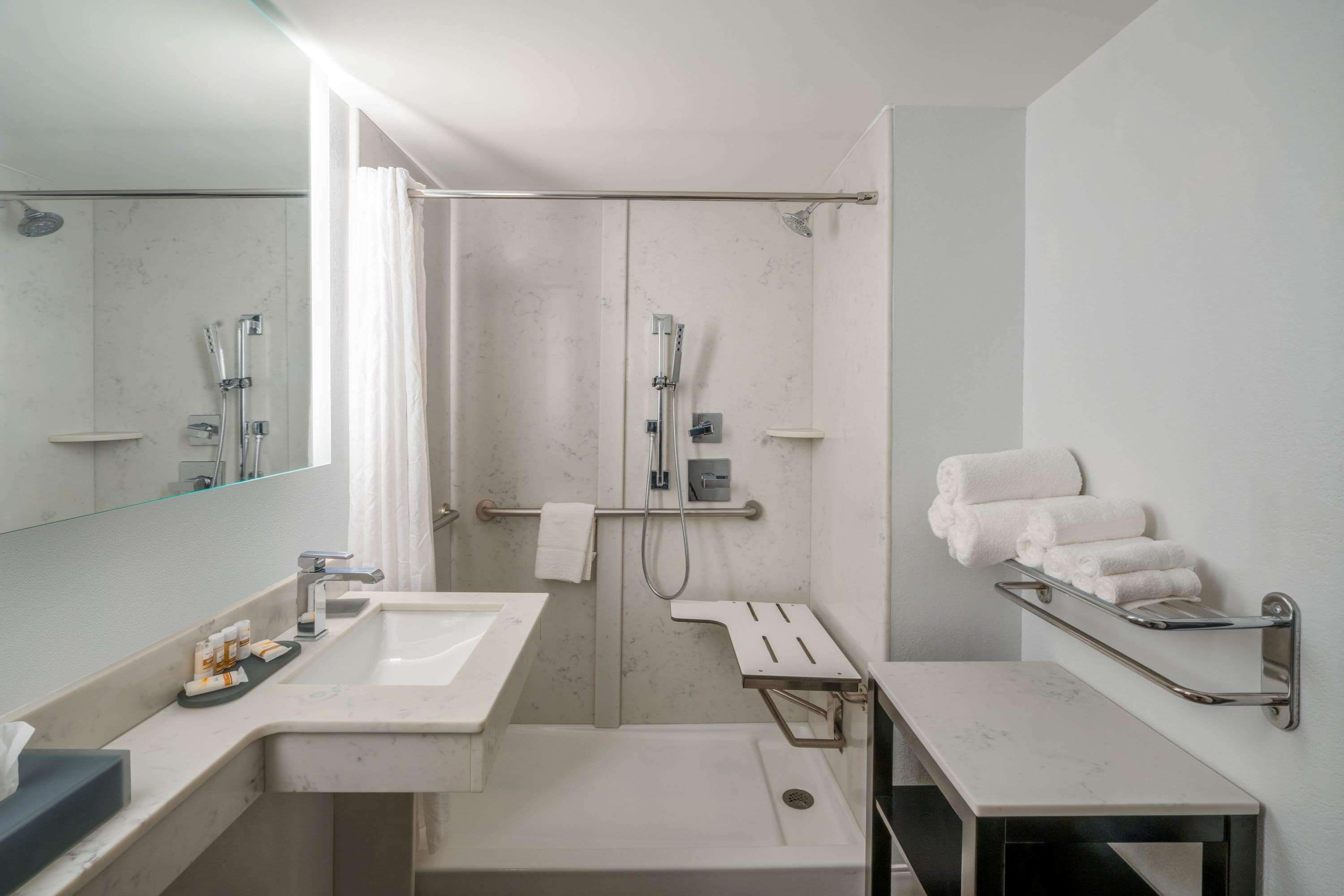 Une salle de bain moderne avec un grand miroir, un lavabo, une douche et un porte-serviettes.