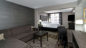 A hotel room with a sofa, a small table, a bed, a desk, a chair, a TV, and a lamp. - La Quinta Inn & Suites by Wyndham Raleigh Downtown North (Raleigh)