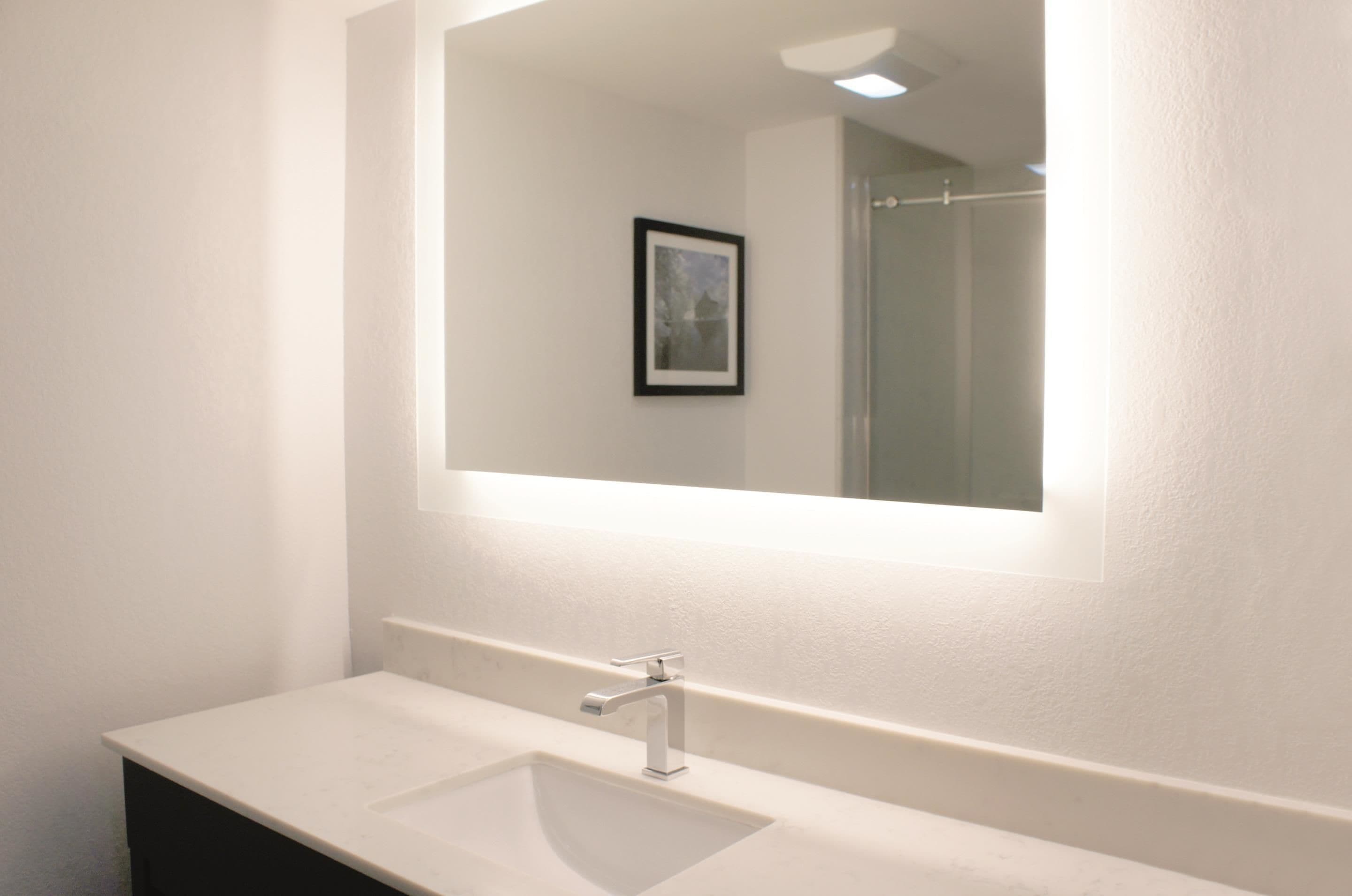 Une salle de bain avec un lavabo blanc, un miroir et un tableau encadré au mur.