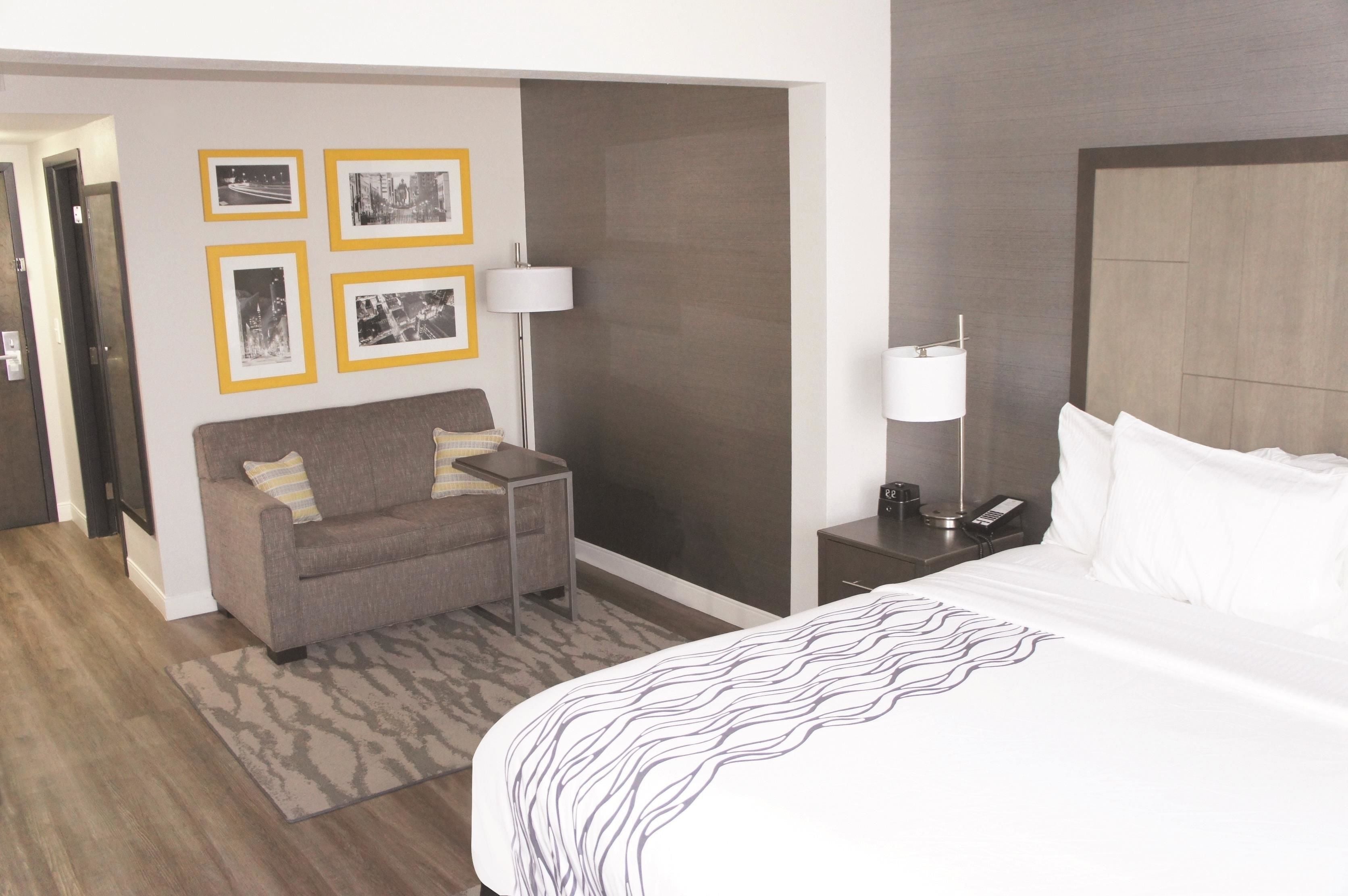 A hotel room with a bed, a sofa, a small table, a lamp, and framed pictures on the wall.