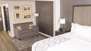 A hotel room with a bed, a sofa, a small table, a lamp, and framed pictures on the wall.