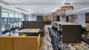 A modern hotel lobby with a bar area, seating arrangements, and large windows providing natural light. - La Quinta Inn & Suites by Wyndham Raleigh Downtown North (Raleigh)