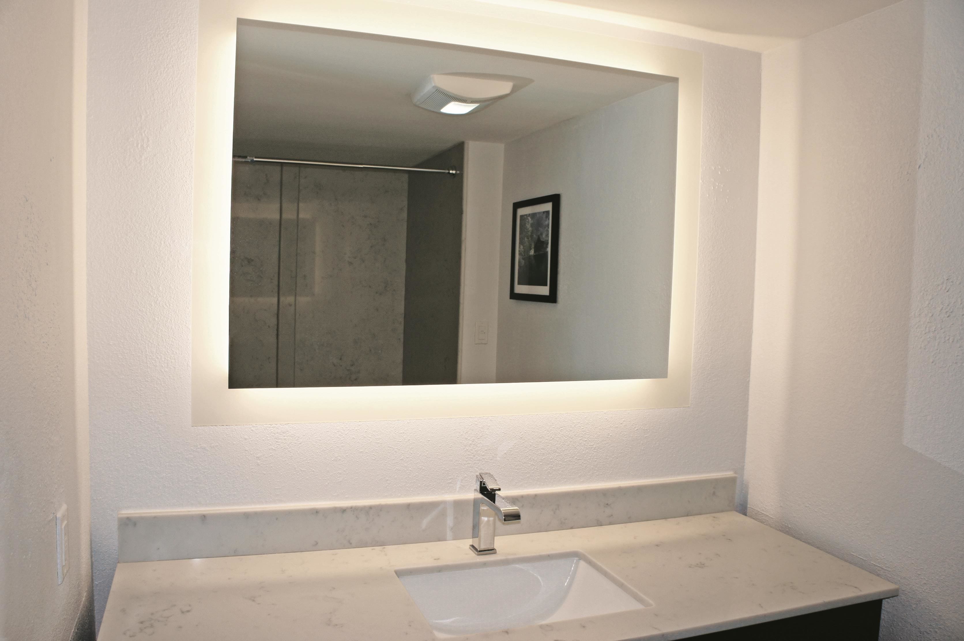 A bathroom with a white sink, a mirror, and a shower visible in the reflection.
