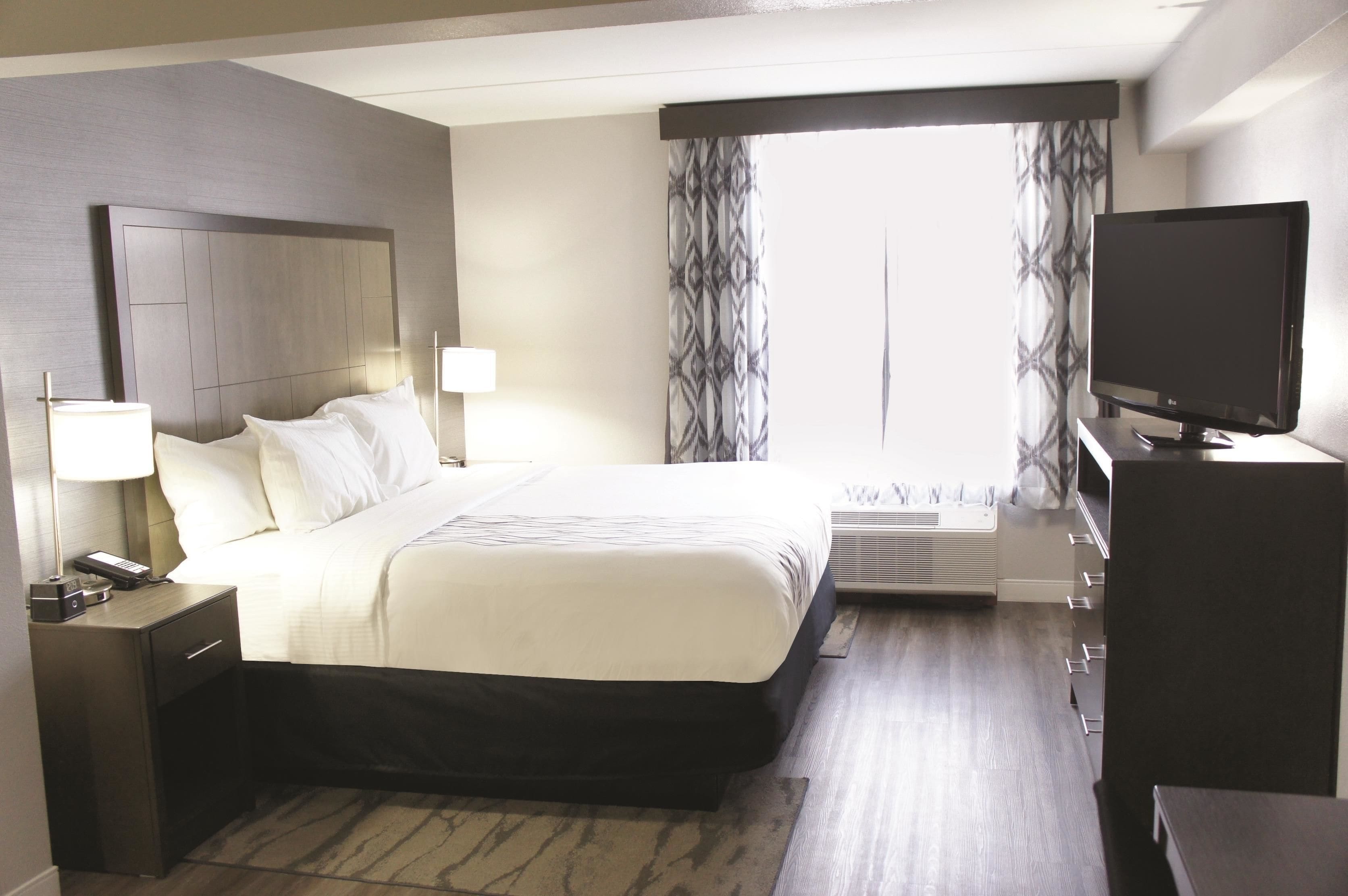 A hotel room with a large bed, bedside lamps, a flat-screen TV, and a window with patterned curtains.