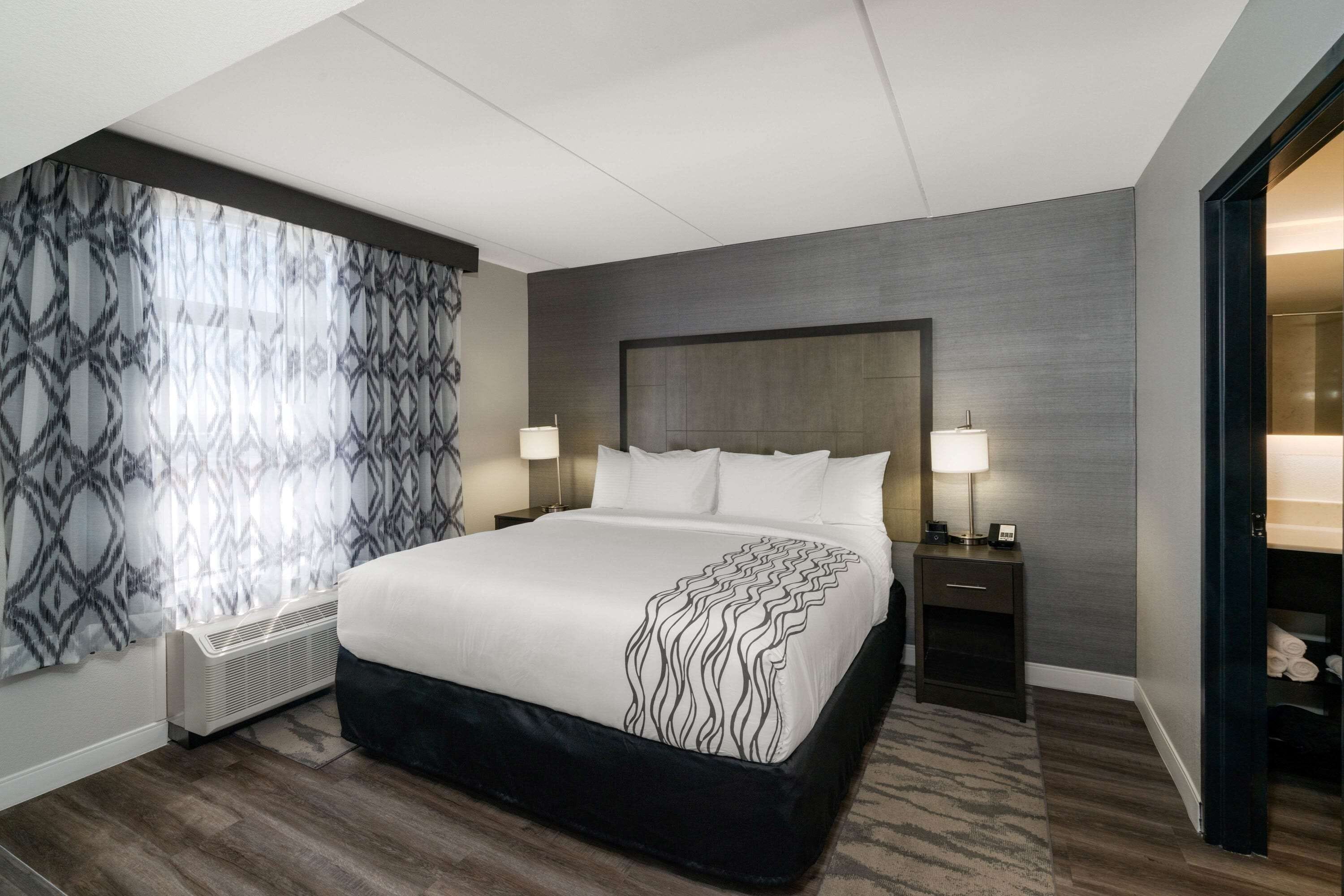A modern hotel room with a large bed, two bedside tables with lamps, a built-in heater, and a wardrobe with a mirror.