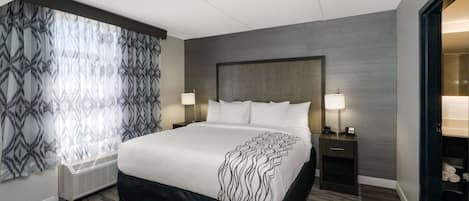 Una habitación de hotel moderna con una cama grande, dos mesitas de noche con lámparas, un calefactor empotrado y un armario con espejo.