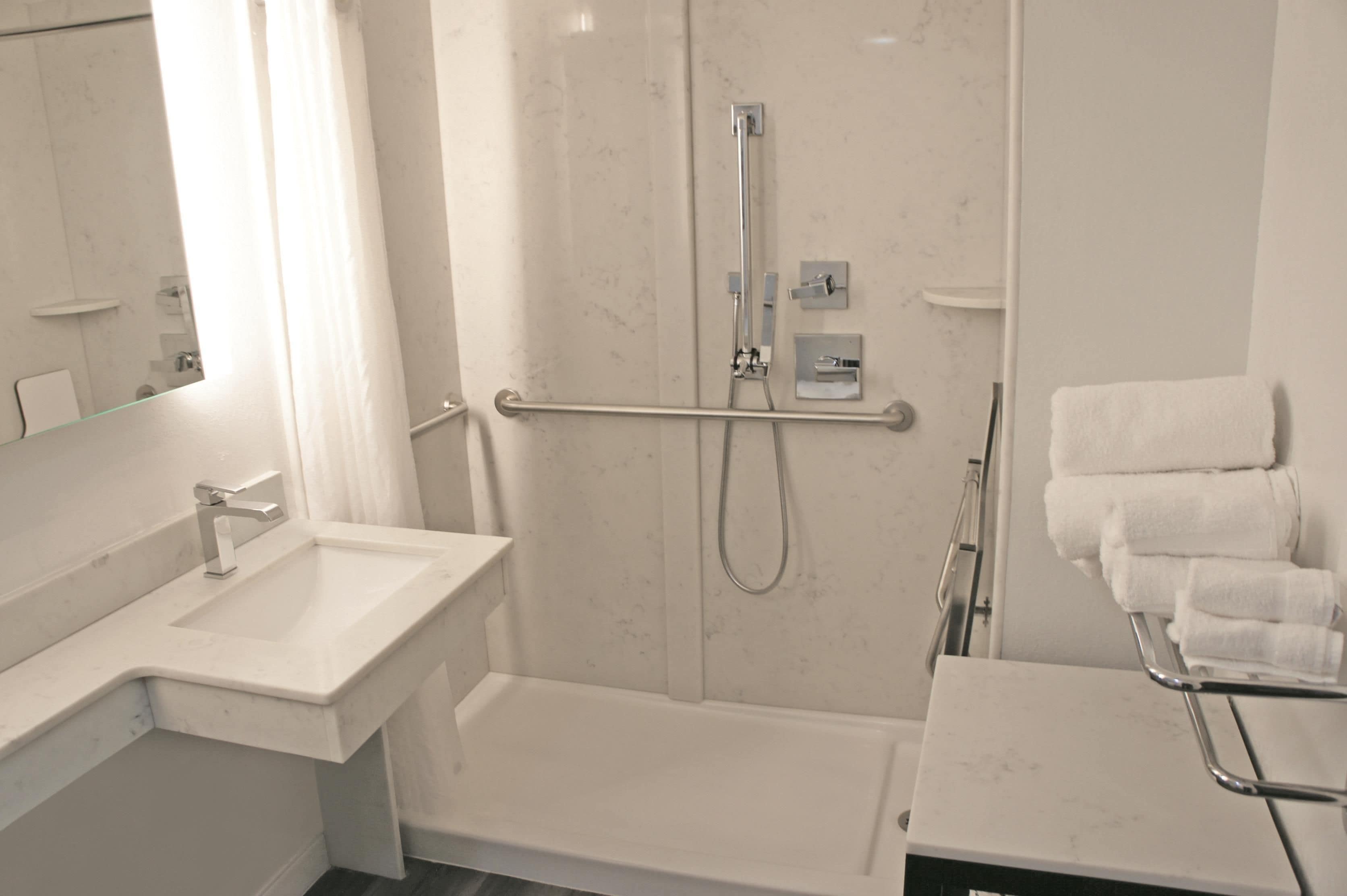A modern bathroom with a white sink, a shower with a grab bar, and a towel rack with folded towels.