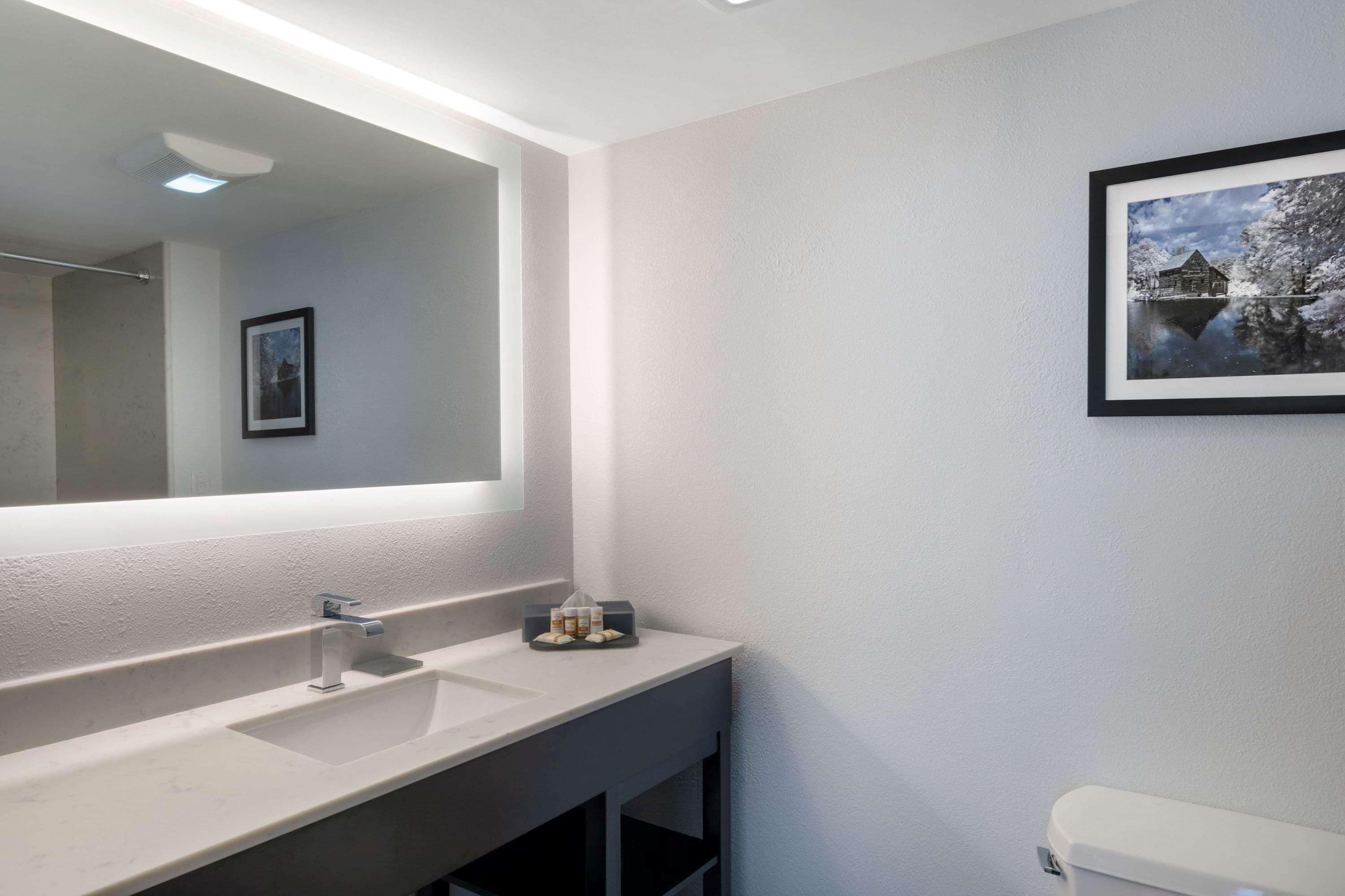 A modern bathroom with a large mirror, a sink, and a toilet.
