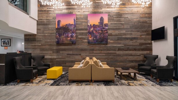 A lobby with a modern design, featuring a reception desk, seating area with sofas and armchairs, and two cityscape paintings on the wall. - La Quinta Inn & Suites by Wyndham Raleigh Downtown North (Raleigh)