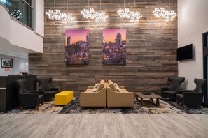A lobby with a modern design, featuring a reception desk, seating area with sofas and armchairs, and two cityscape paintings on the wall. - La Quinta Inn & Suites by Wyndham Raleigh Downtown North (Raleigh)