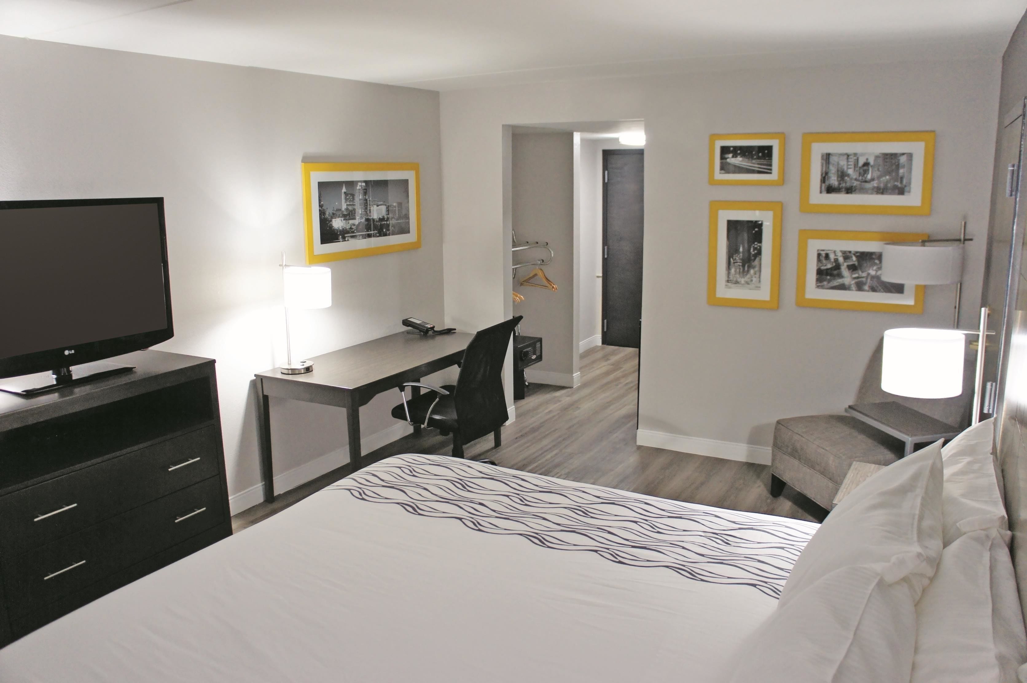 A hotel room with a bed, a desk, a chair, a TV, and framed pictures on the wall.
