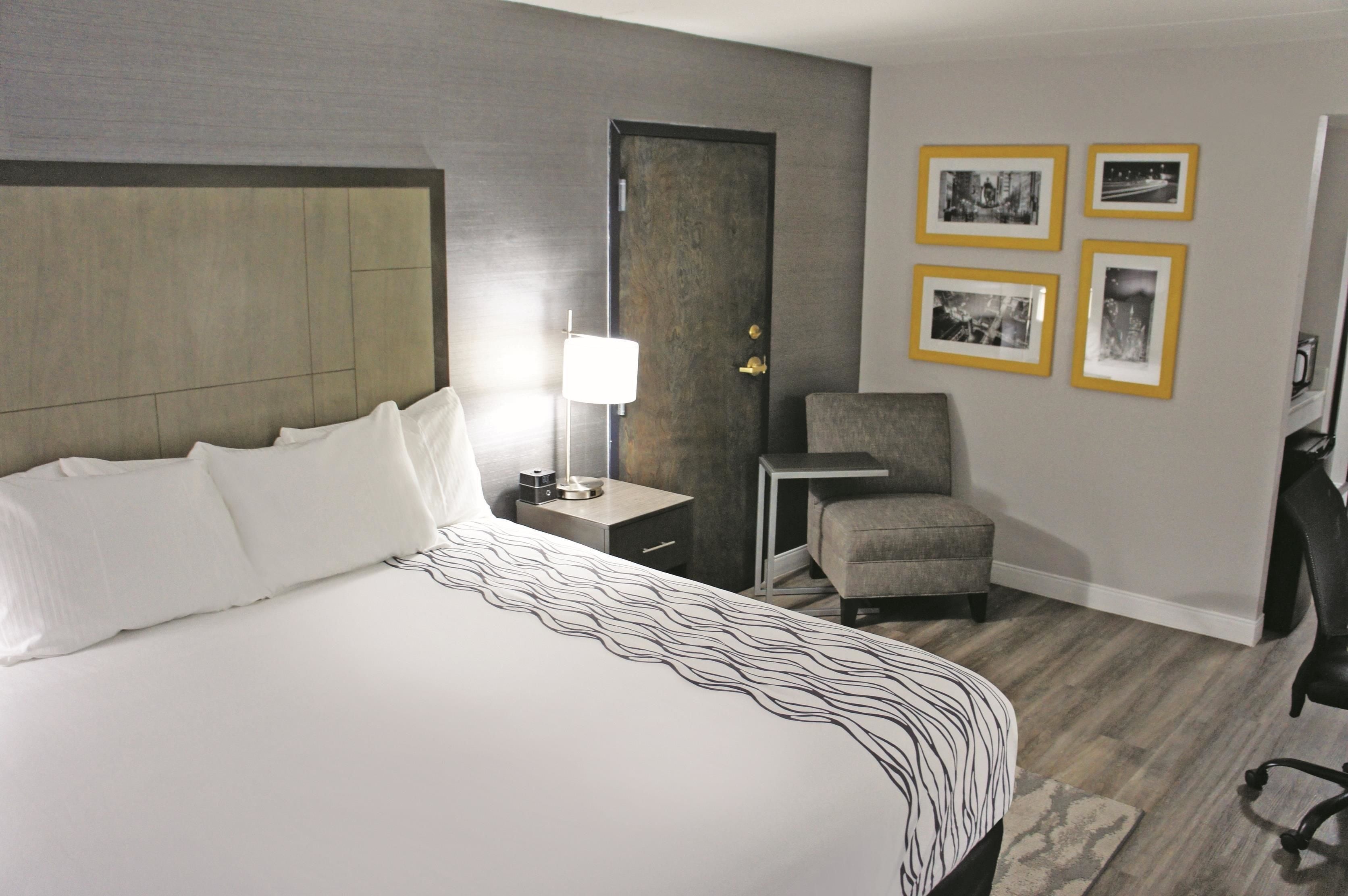 A hotel room with a large bed, a nightstand with a lamp, a chair, and framed pictures on the wall.