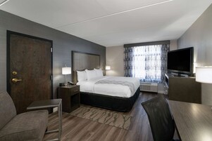 A hotel room with a bed, a TV, a desk, a chair, and a window with curtains.