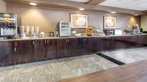 A hotel reception area with a coffee machine, juice dispensers, a microwave, and a fruit display. - Wingate by Wyndham - Joliet (Joliet)