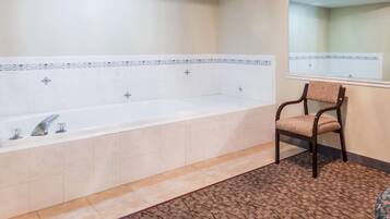 Une salle de bain avec une grande baignoire, une chaise et un tapis à motifs.
