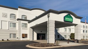 A Wingate by Wyndham hotel with a modern facade, a covered entrance, and an American flag. - Wingate by Wyndham - Joliet (Joliet)