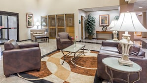 A lobby with leather sofas, a coffee table, a lamp, and a large potted plant. - Wingate by Wyndham - Joliet (Joliet)