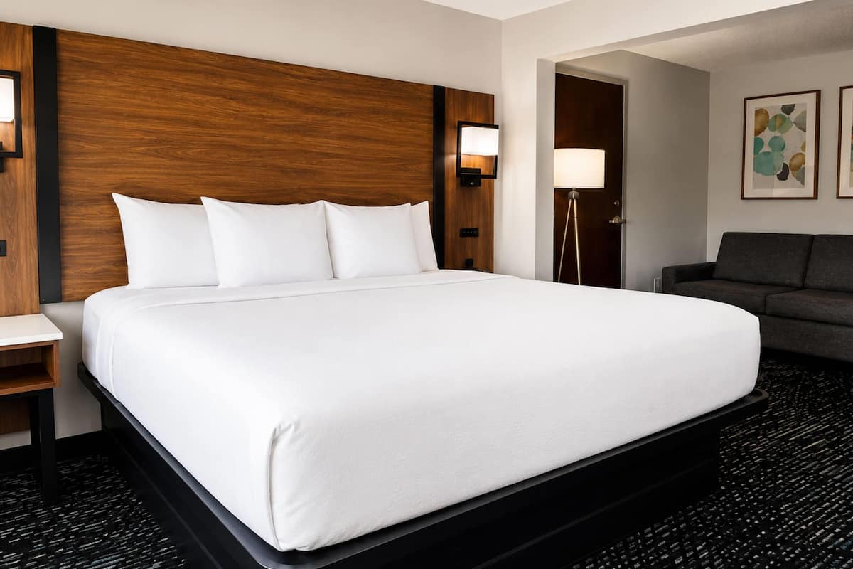 Une chambre d’hôtel avec un grand lit, une table de chevet, une lampe, un canapé et des œuvres d’art accrochées au mur.