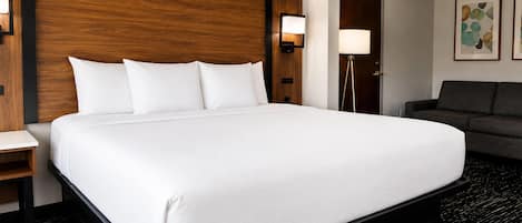 A hotel room with a large bed, a bedside table, a lamp, a sofa, and artwork on the wall.