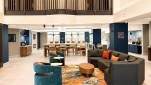 Un hall d’entrée spacieux avec un plafond haut, une mezzanine, un coin repas et un espace détente agrémenté d’un tapis à motifs.