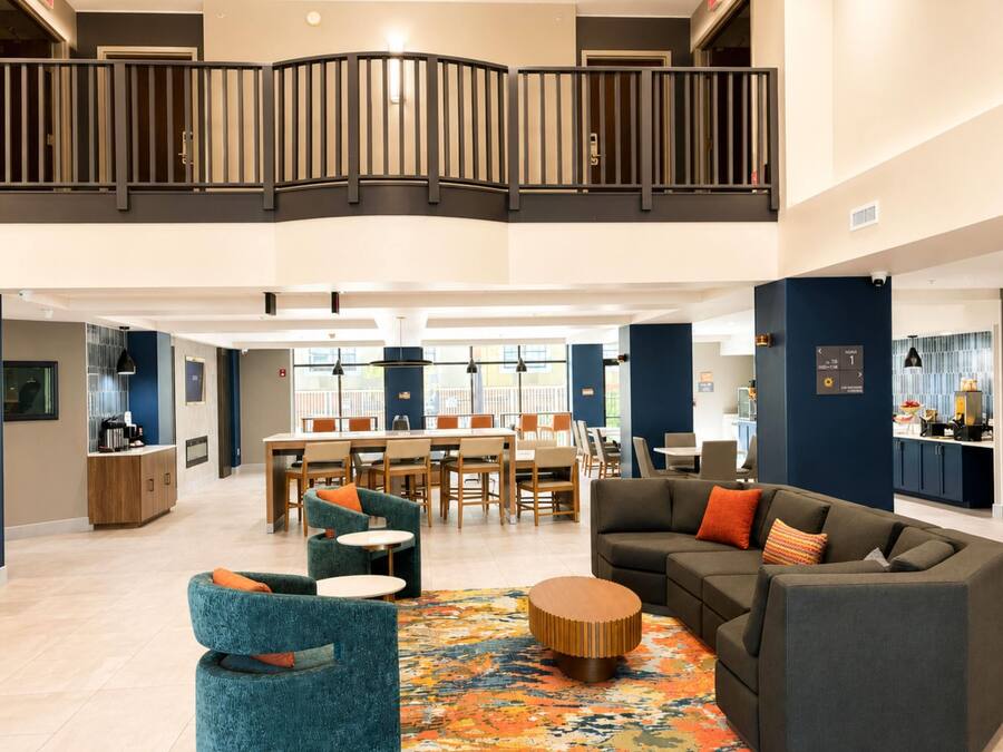 A spacious lobby with a high ceiling, a mezzanine level, a dining area, and a seating area with a patterned rug.