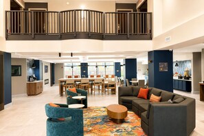 En rummelig lobby med højt til loftet, en mezzanin, et spiseområde og et siddeområde med et mønstret tæppe.
