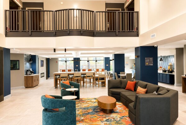 Un hall d’entrée spacieux avec un plafond haut, une mezzanine, un coin repas et un espace détente agrémenté d’un tapis à motifs.