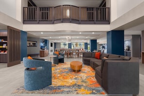 A spacious lobby with a high ceiling, a dining area, and a kitchen visible in the background.