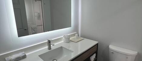 A modern bathroom with a large mirror, a white sink, a toilet, and a towel rack.