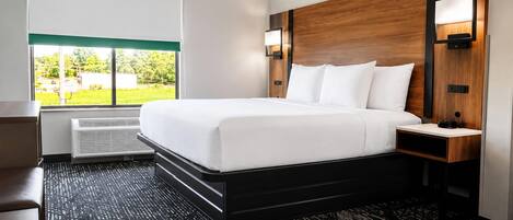 Habitación de hotel con una cama grande, un escritorio, una silla, una ventana con vistas y una lámpara de pared.