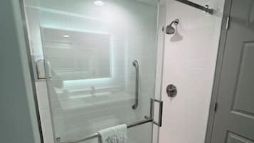 A glass-enclosed shower with a towel rack, a handheld showerhead, and a toilet paper holder.