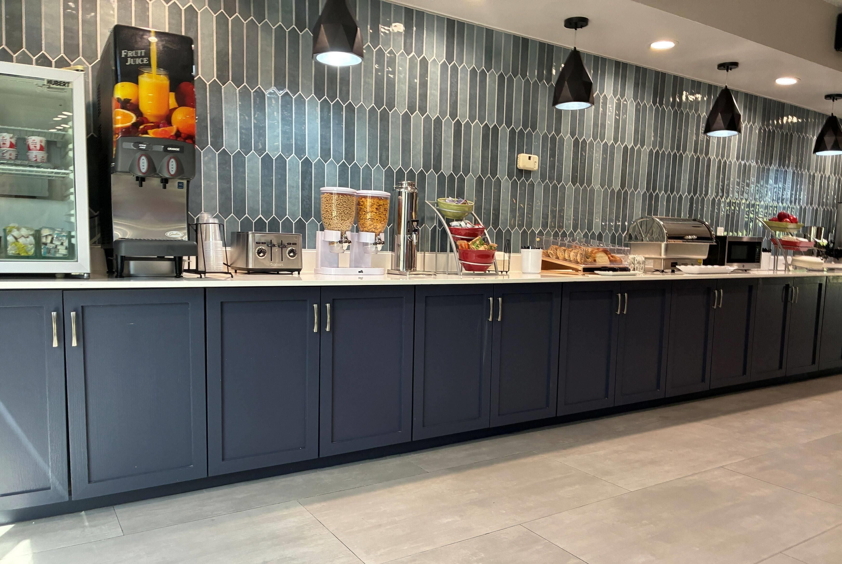 A modern breakfast bar with a juice dispenser, coffee machines, and a variety of food items.