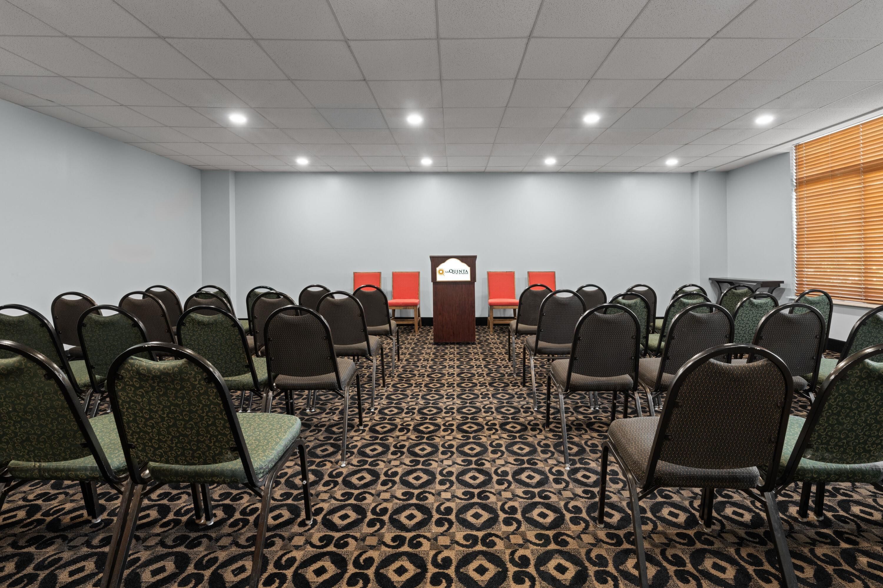 A conference room with rows of chairs, a podium, and a carpeted floor.
