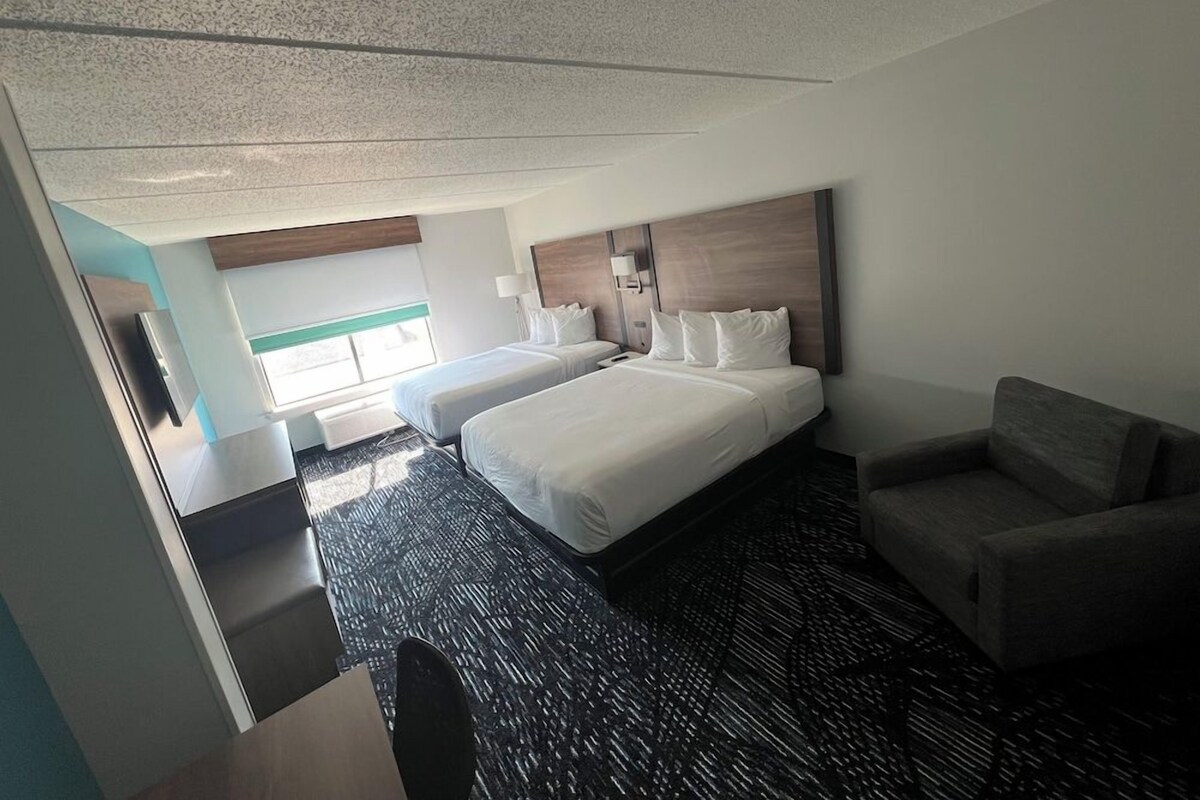 Habitación de hotel con dos camas, un escritorio, una silla y un ventanal grande.