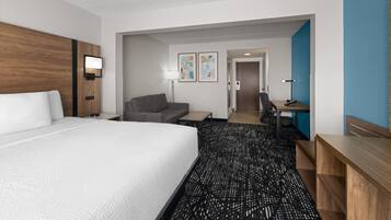 A hotel room with a large bed, a desk, a chair, a sofa, and a small table.