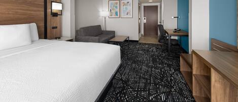 A hotel room with a large bed, a desk, a chair, a sofa, and a small table.