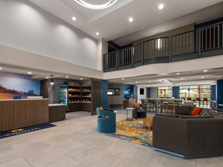 A spacious lobby with a reception desk, a seating area with a sofa and chairs, a staircase, and a dining area with tables and chairs.