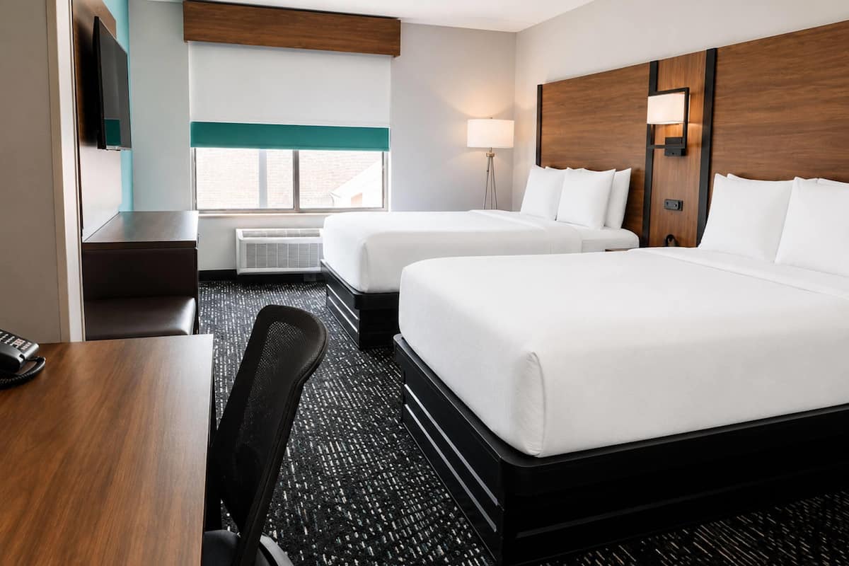 Une chambre d’hôtel avec deux lits, un bureau, une chaise, une télévision, une fenêtre et une lampe.