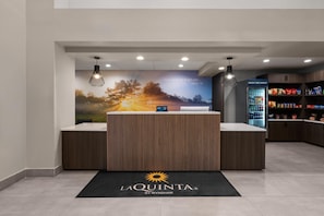 A reception area with a wooden reception desk, a refrigerator stocked with beverages, and a wall with a scenic image and text.