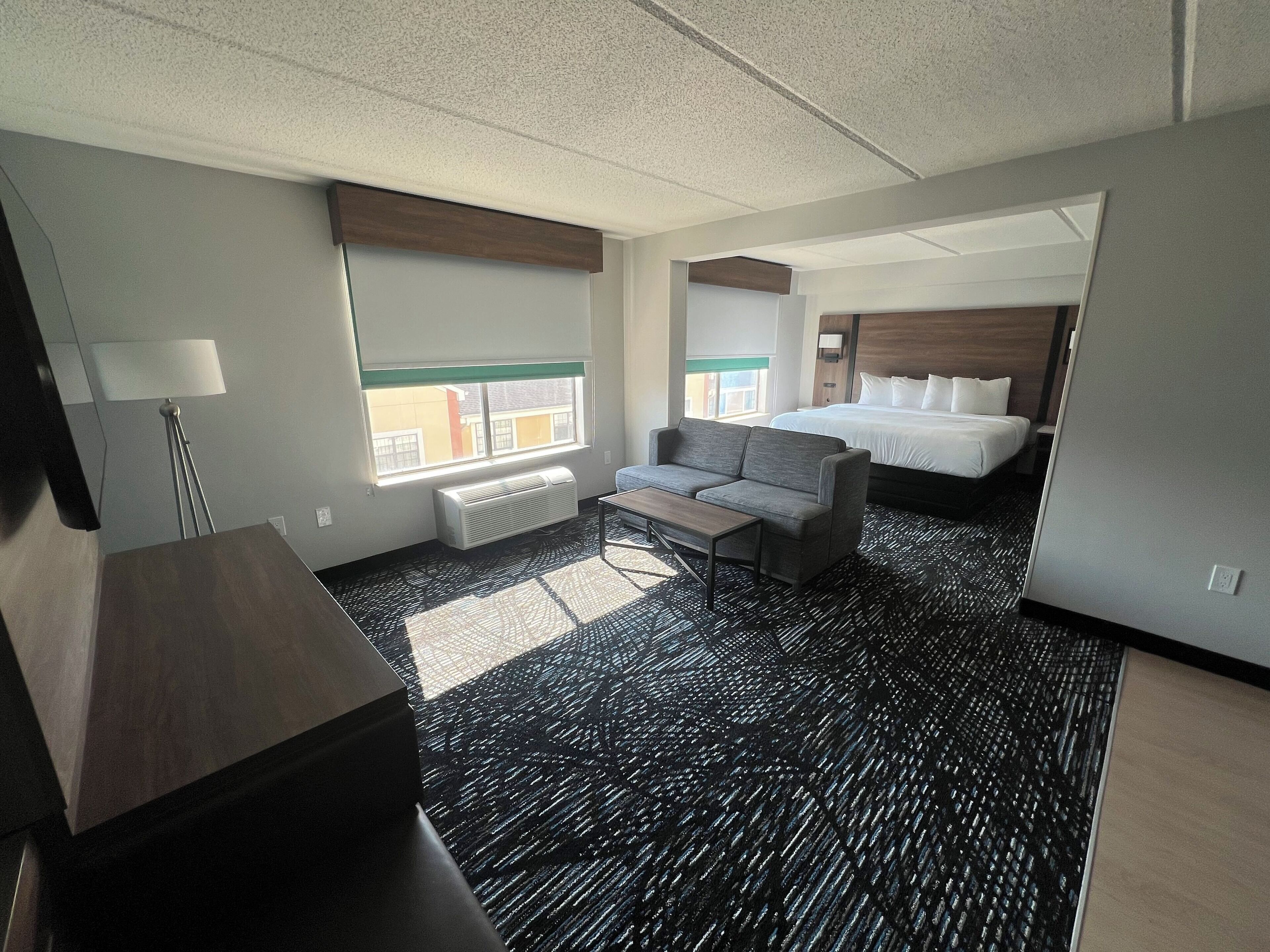 A hotel room with a large bed, a sofa, a desk, and a window with a view of buildings outside.