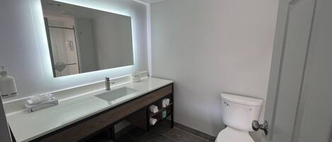 A modern bathroom with a large mirror, a sink, and a toilet.