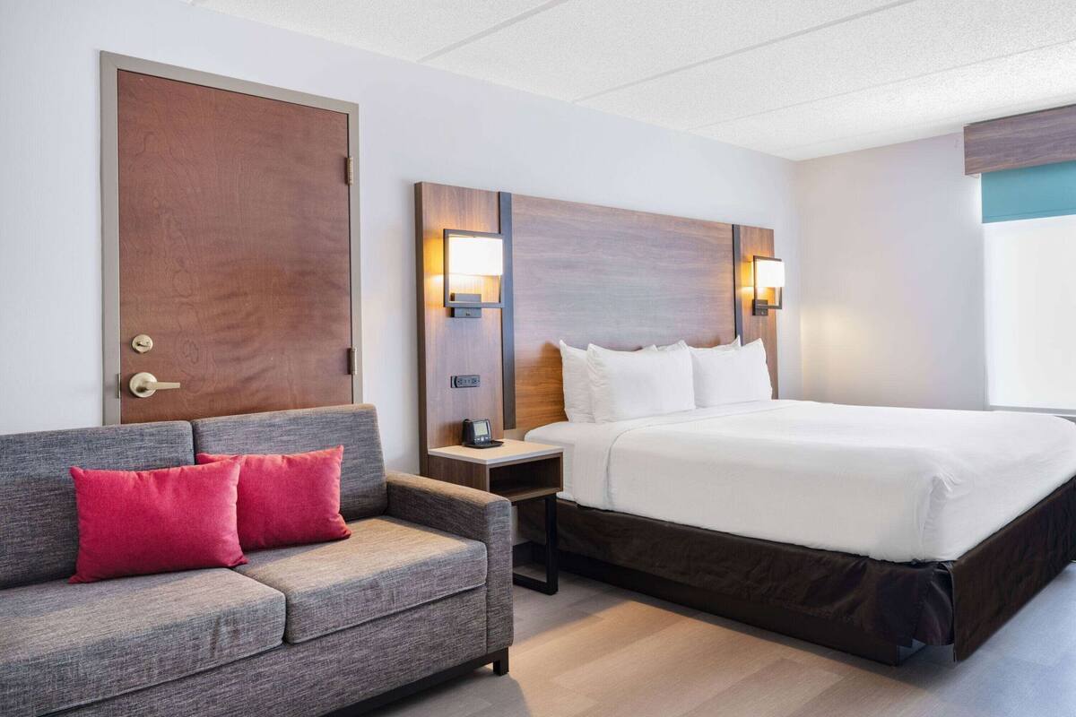 Une chambre d’hôtel comprenant un lit, un canapé, une table de chevet et une lampe fixée au mur.