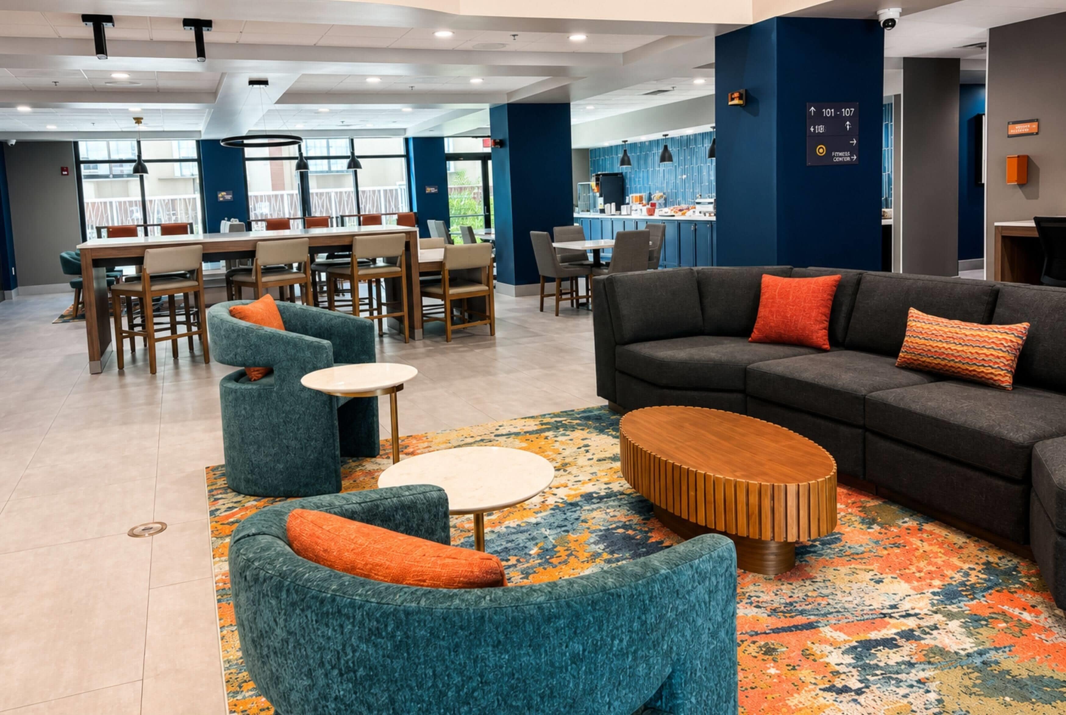 A modern hotel lobby with a seating area, a bar, and a fitness center direction sign.