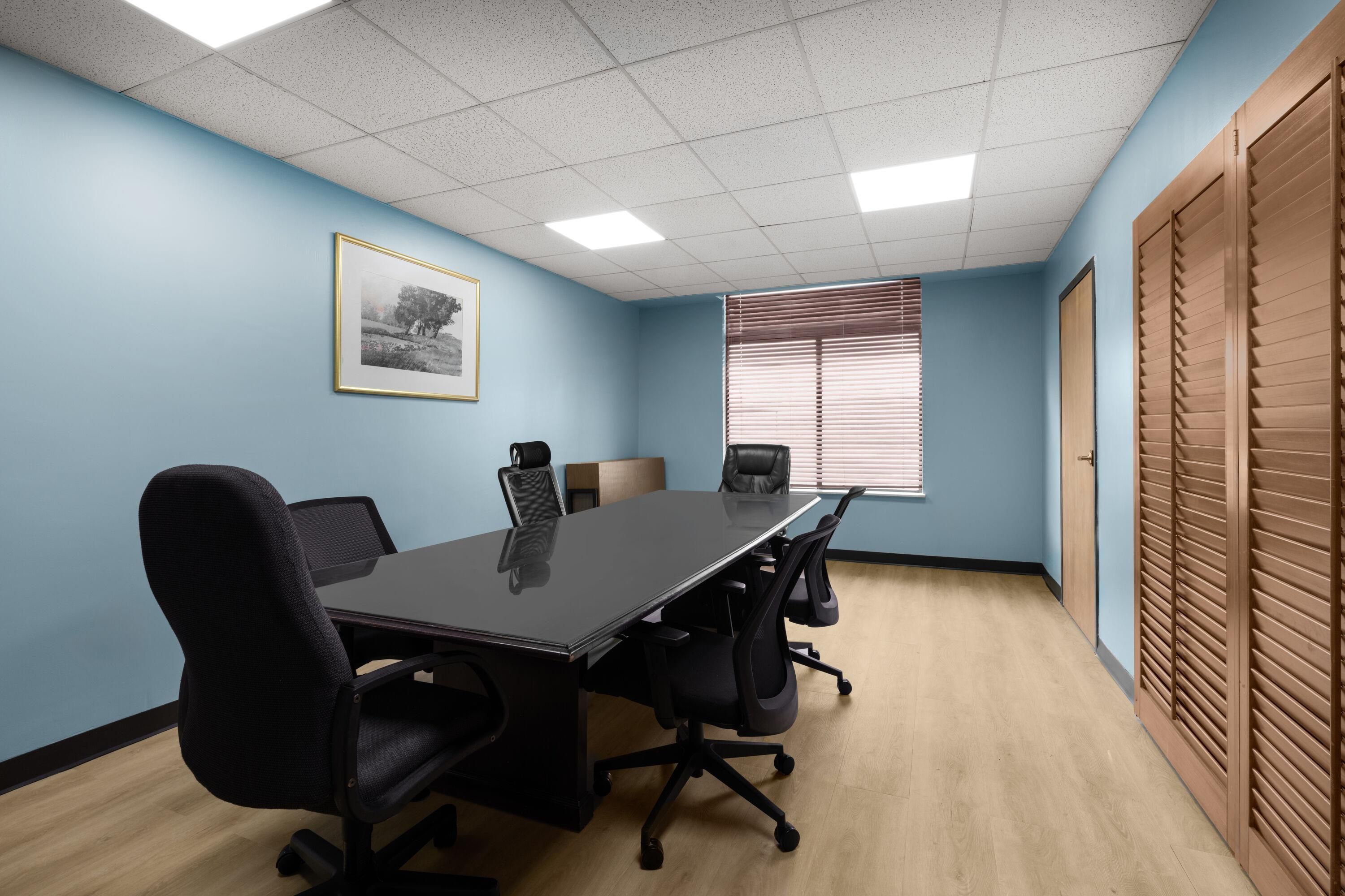 A conference room with a long table, four chairs, a framed picture on the wall, and a window with blinds.