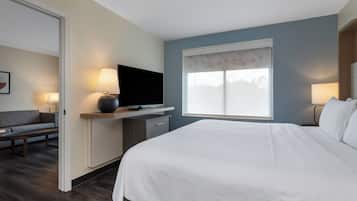 A hotel room with a bed, a TV on a stand, a desk, a chair, and a window with a view.