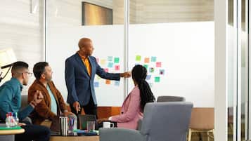 A meeting room with a glass wall, a whiteboard with sticky notes, and a table with laptops and pens.